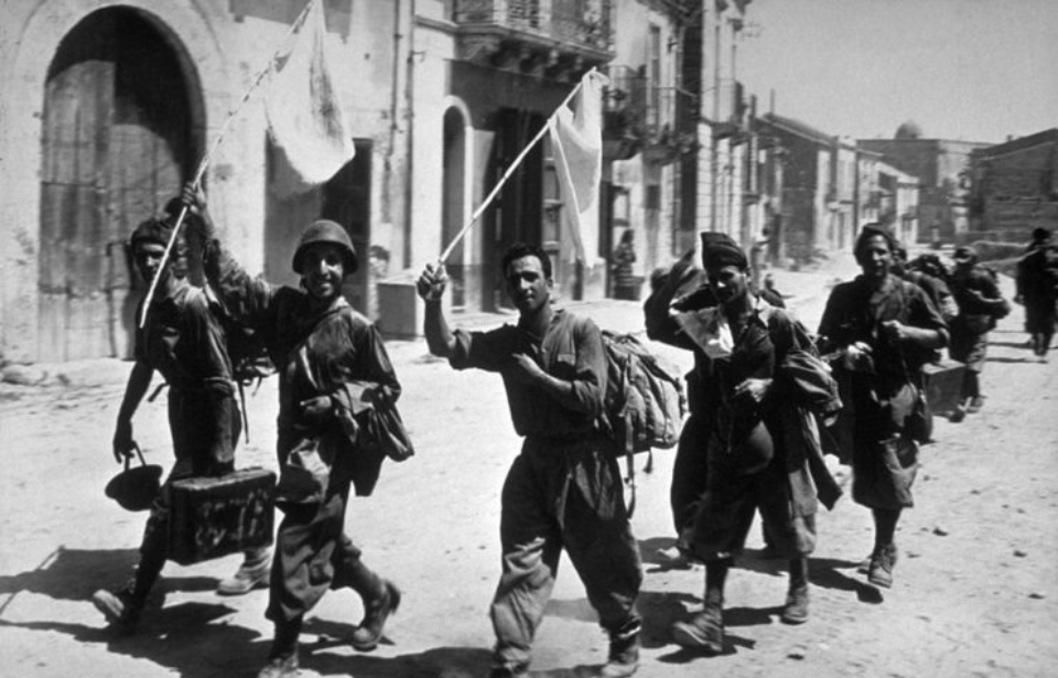 Italian soldiers walking down a street while waving white flags