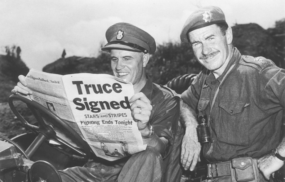 Two commanding officers reading a newspaper announcing the armistice being signed to pause the Korean War