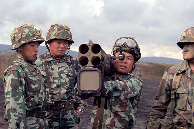 Japanese soldier manning an M202A1 FLASH while two other Japanese soldiers and one US infantryman stand watch