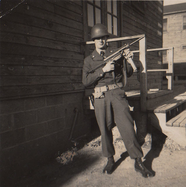 Soldier holding an M3 "Grease Gun" while standing outside a building