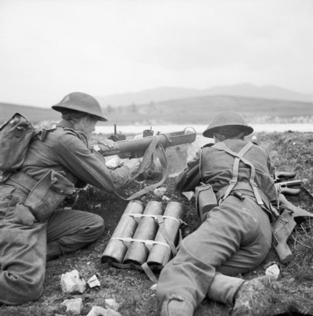 Two soldiers lying it a low trench with weapons and ammunition