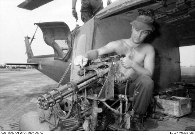 Raymond Basil Hawkins sitting in a grounded helicopter while examining an M134 Minigun
