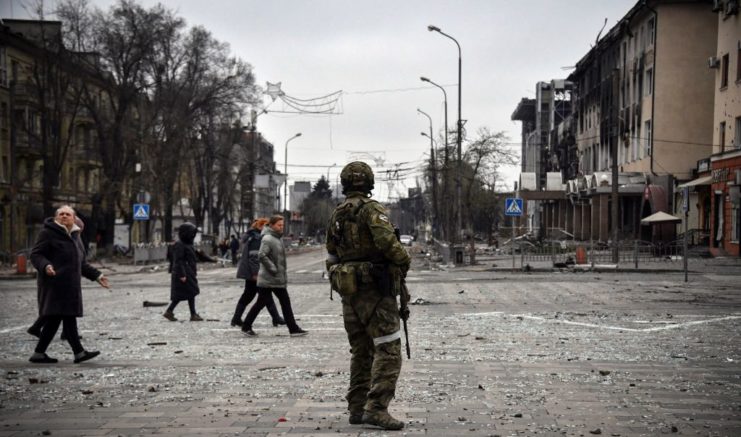 Residents walking by a Russian soldier standing in the middle of a street