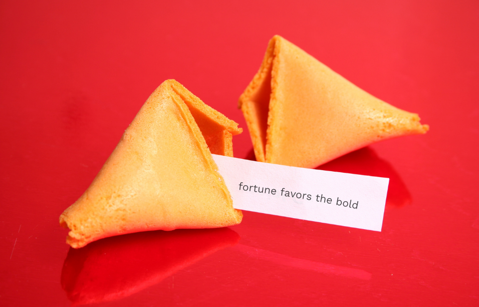 Fortune cookie cracked open with a slip of paper reading "fortune favors the bold"