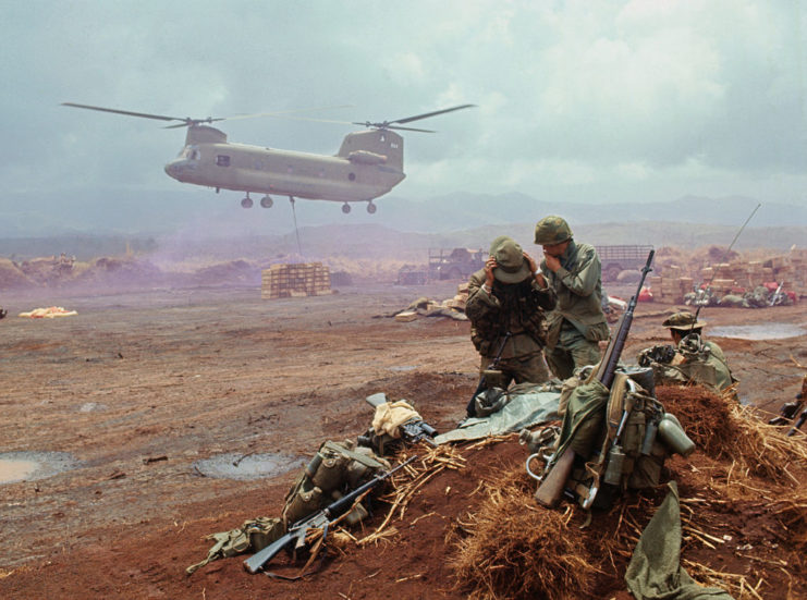 Chinook helicopter landing while US soldiers stand together in the distance