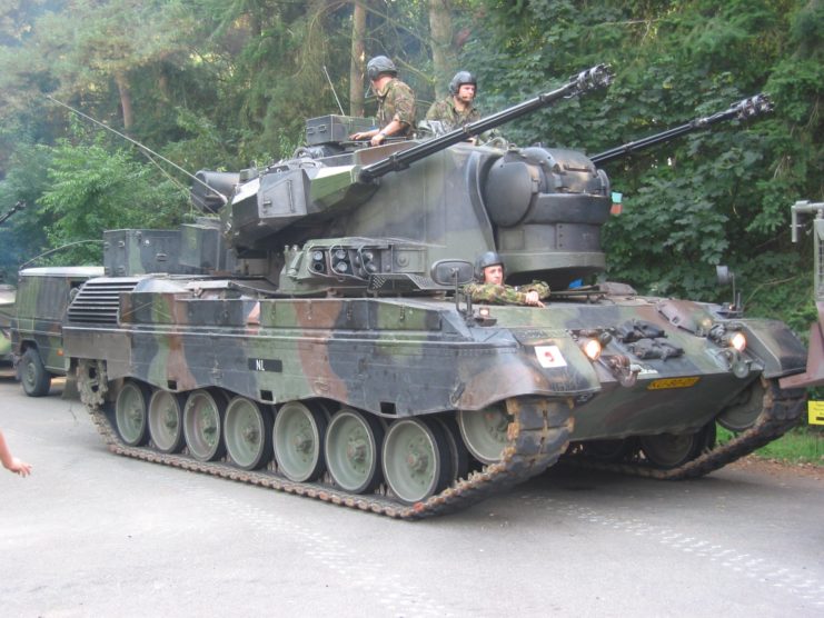 Dutch soldiers half-sitting in a Flakpanzer Gepard driving along a road