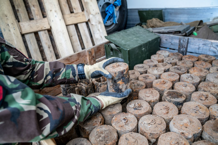 Soldier holding an S-mine over a boxed filled with dirt-covered mines