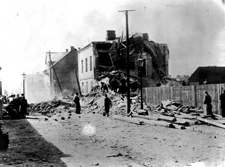 People walking by a damaged building along a debris-laden street