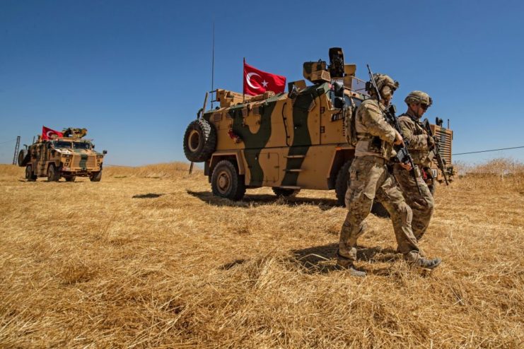 Turkish military troops walking alongside two military vehicles