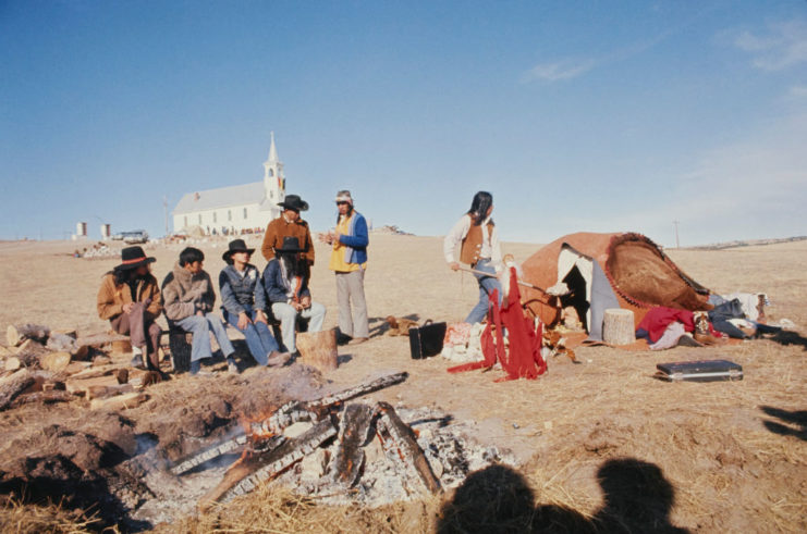 Group of American Indian Movement activists standing around a fire and tent