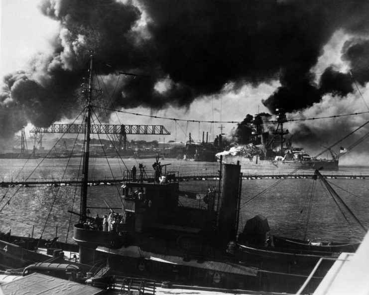 Port installation and the USS Nevada (BB-36) shrouded in smoke