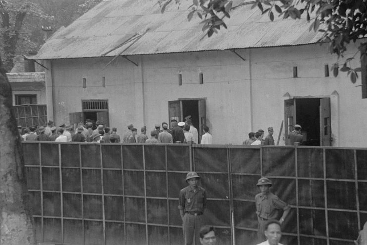 Prisoners of war (POWs) gathered behind a fence that's guarded by soldiers