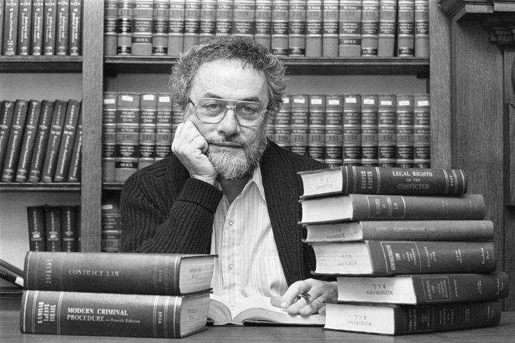 Adrian Cronauer sitting with stacks of books on his desk