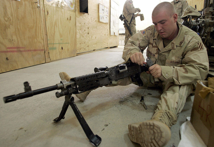 US service member holding the back of an M240 while sitting down