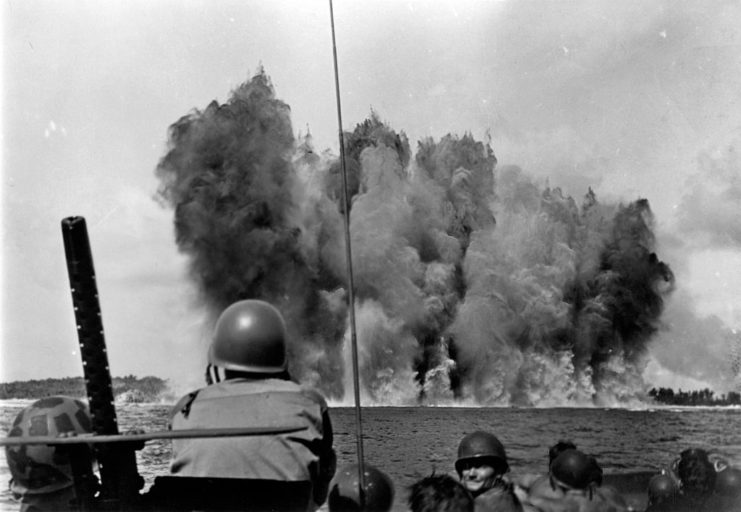 US troops watching an explosion happen near an island's shore