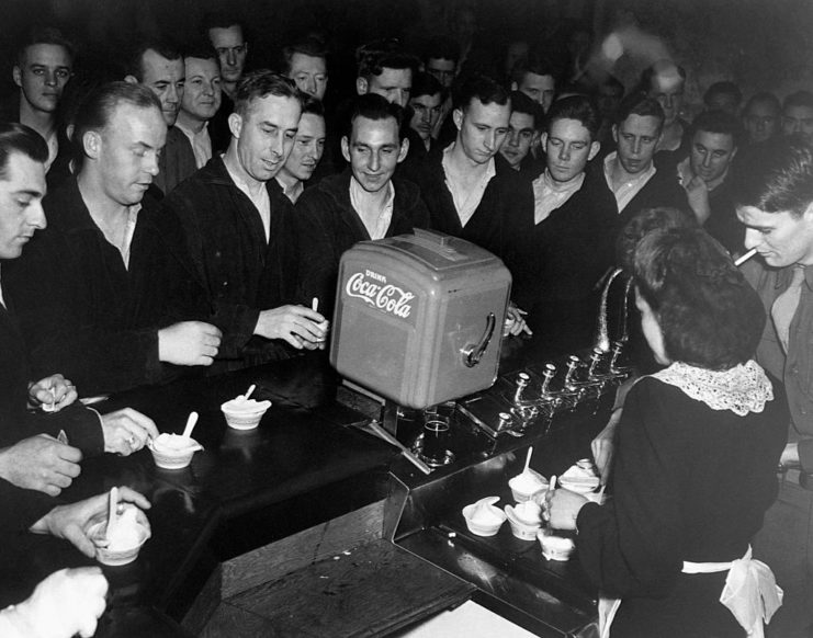 US soldiers gathered around a woman passing out bowls of ice cream