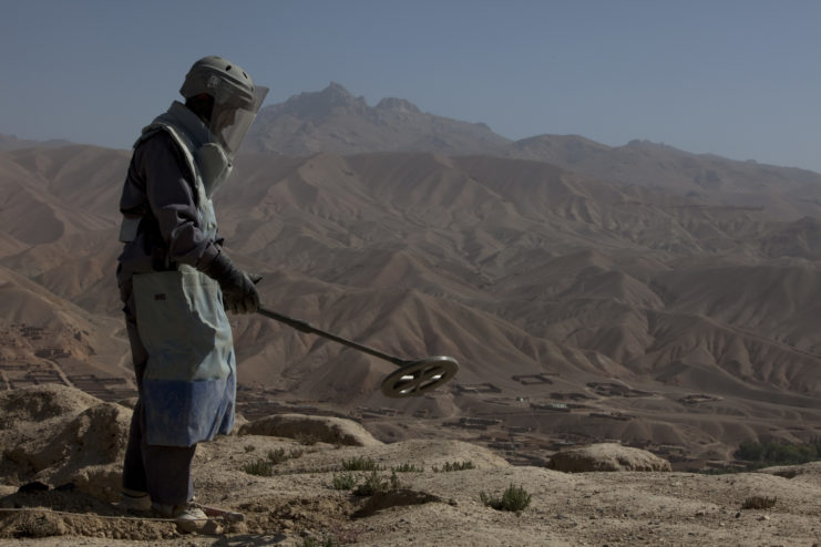 De-miner hovering a mine detector over the Shahr-e Gholghola archaeological site