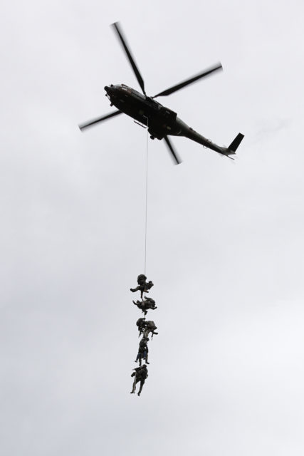 GIGN team members hanging from a rope below a hovering helicopter