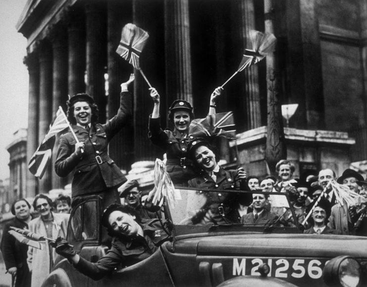 Members of the Auxiliary Territorial Service (ATS) waving flags while riding in a service vehicle