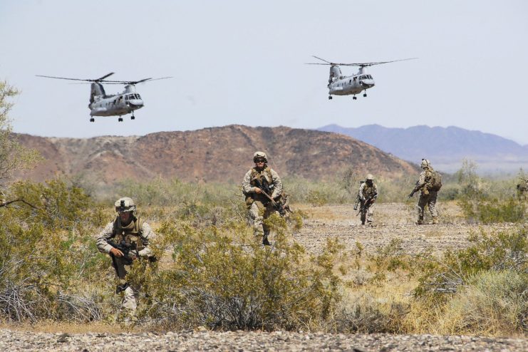 Four US Marines running through Yuma Proving Ground while two helicopters fly overhead