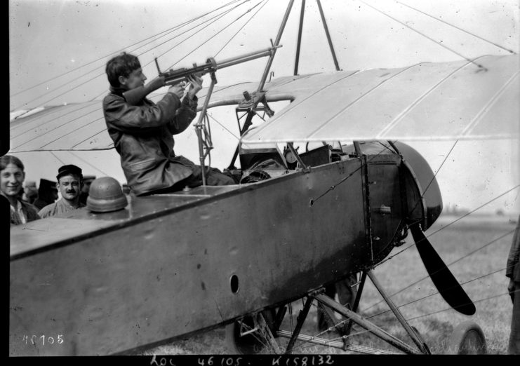 Georges Guynemer aiming a rifle while sitting in the cockpit of a grounded Morane-Saulnier L