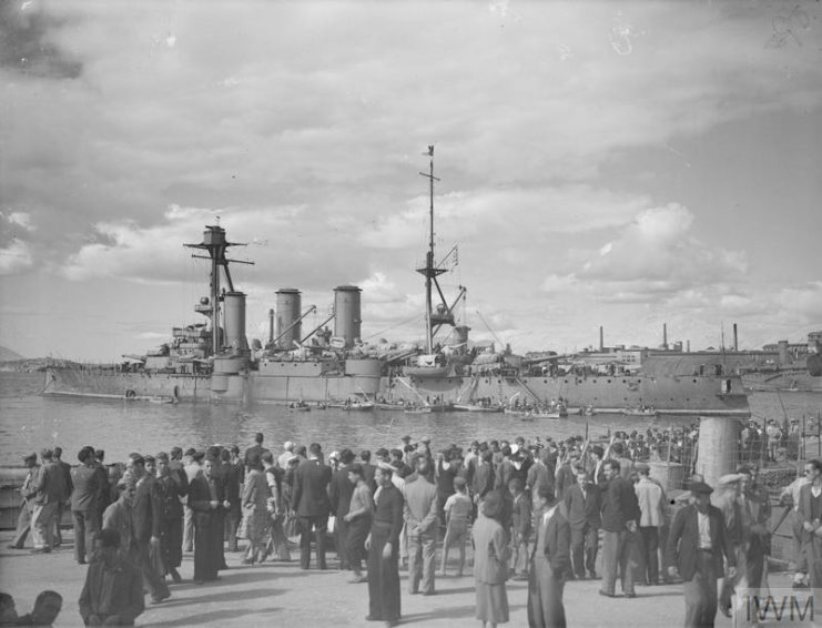 Crowd gathered on a dock, with Georgios Averof anchored in the distance