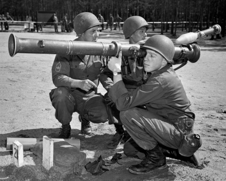 Soldier manning a bazooka while two others prepare ammunition