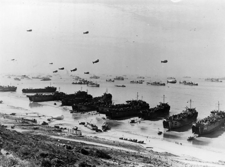 Barrage balloons and ships anchored along the shore of Omaha Beach