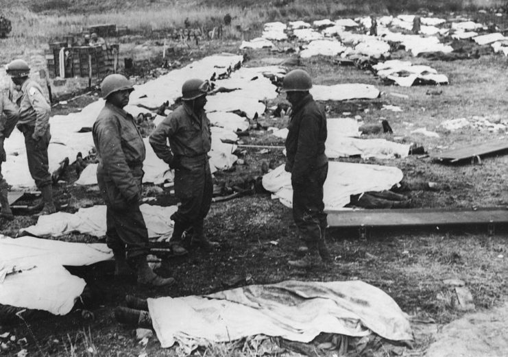 Medical orderlies standing among dead bodies covered with white sheets