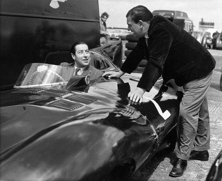 Tony Rolt sitting in a Jaguar while Duncan Hamilton leans over to speak with him