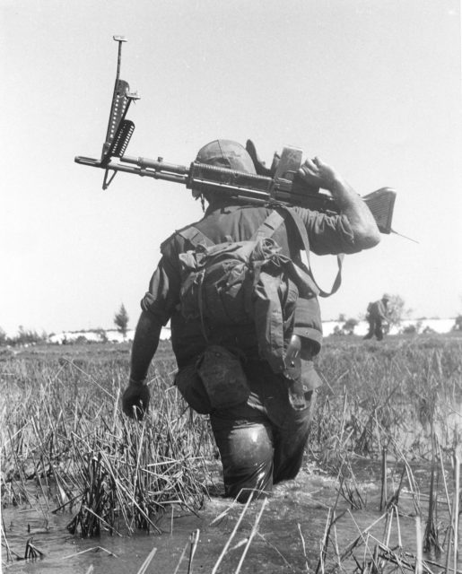 American soldier wading through a rice paddy while holding an M60 machine gun