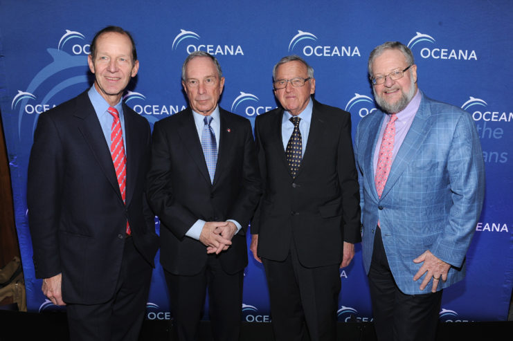 Theodore Roosevelt IV, Michael Bloomberg, Hansjorg Wyss, and David Rockefeller wearing suits stand in front of a blue curtain with the Oceana logo.