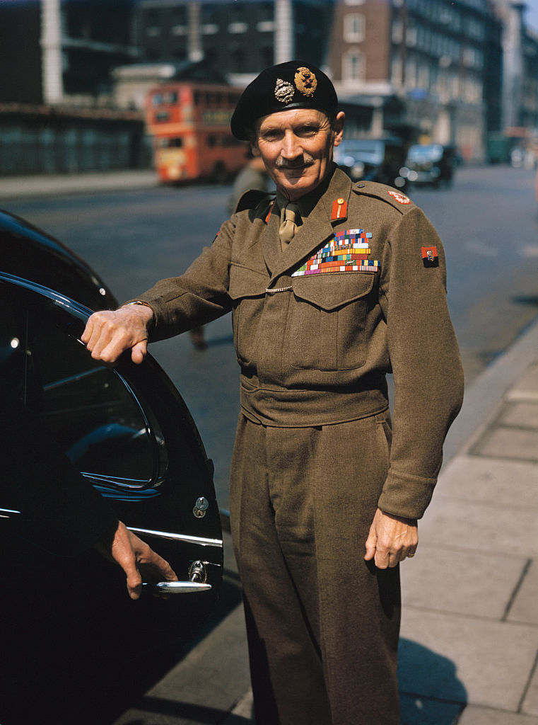 Bernard Law Montgomery wearing military dress standing with his hand on an open car door.