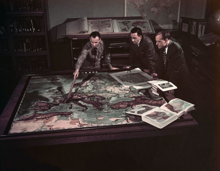 Three US military officials looking over a map spread across a table