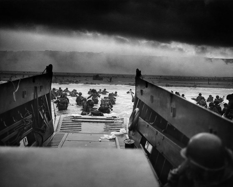 American troops disembarking a landing craft and wading through water toward shore
