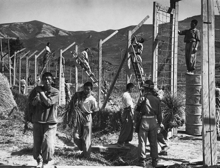 Prisoners walking near the fence of a prisoner of war (POW) camp