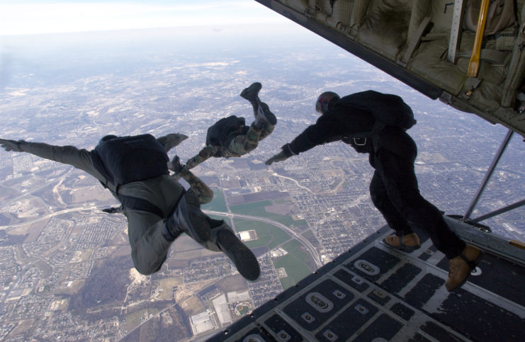 Three US Air Force airmen jumping out of the rear of an aircraft