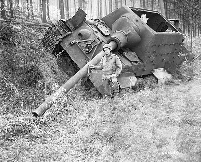 Soldier standing beside a Jagdtiger positioned on the side of a small incline