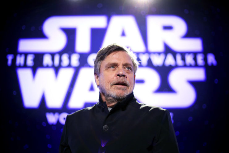 Mark Hamill standing in front of an illuminated screen that reads, "STAR WARS: THE RISE OF SKYWALKER"