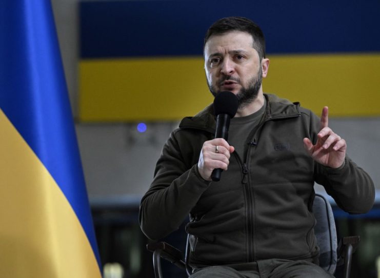 Volodymyr Zelenskyy speaking into a microphone while seated