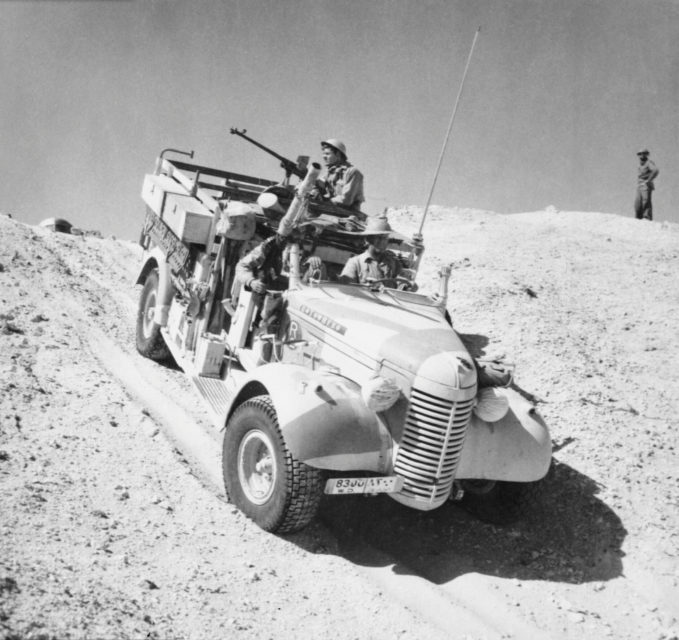 Truck driving down a steep sand dune while a member of the Long Range Desert Group (LRDG) mans the vehicle's machine gun