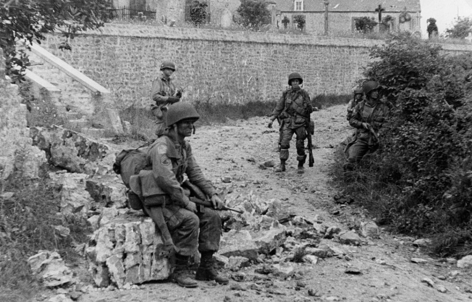 Three American paratroopers standing among rubble