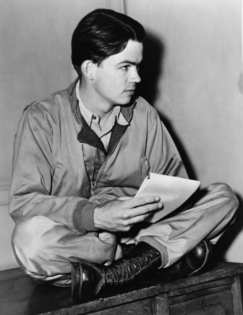 Bill Mauldin sitting crosslegged while holding his notebook