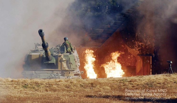 South Korean soldier standing atop a K9 Thunder that's positioned next to large flames
