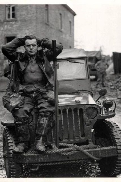 German pilot sitting on the front of a Jeep with his hands behind his head