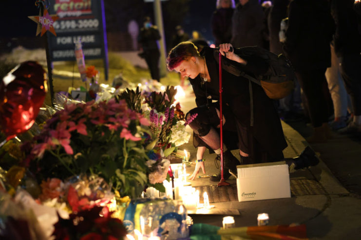 Woman kneeling in front of a makeshift memorial near Club Q