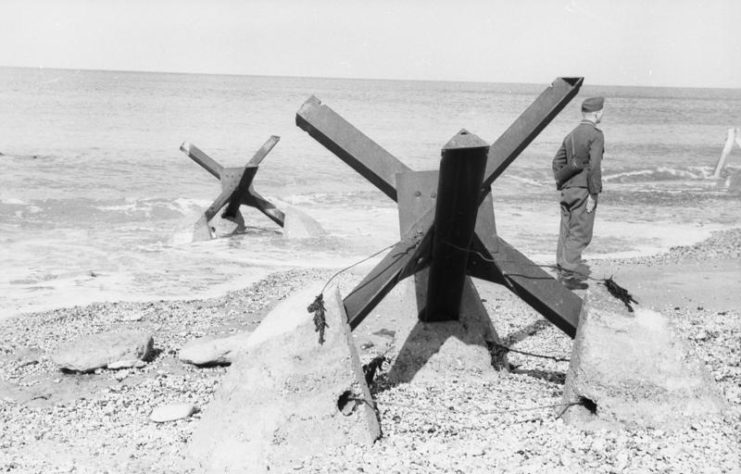 Soldier standing near a Czech hedgehog on a beach