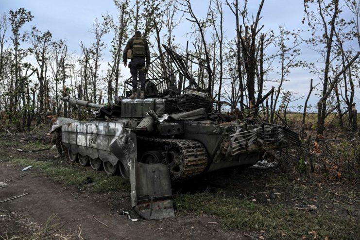 Ukrainian soldier standing atop a damaged Russian tank