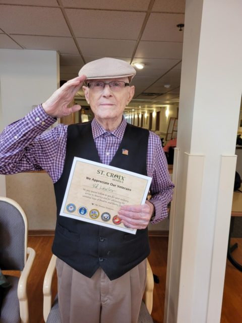 Ed Lawler saluting while holding a certificate in recognition of his service