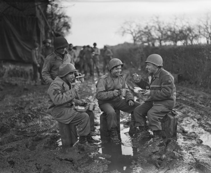 Three US soldiers eating food together in the mud
